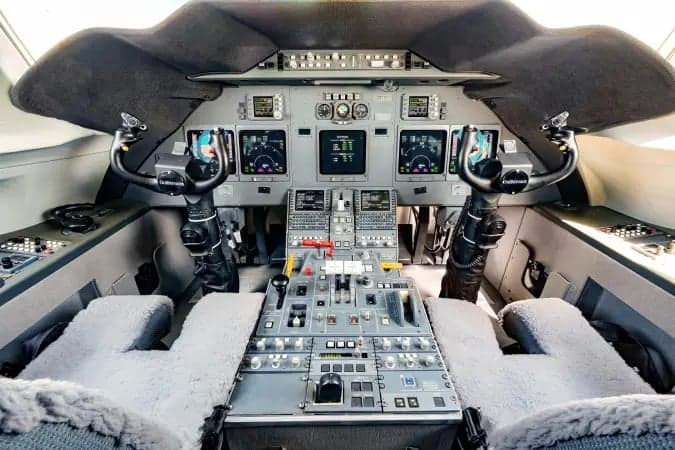 The cockpit of a business jet, featuring multiple display screens, control yokes, and a central control panel.