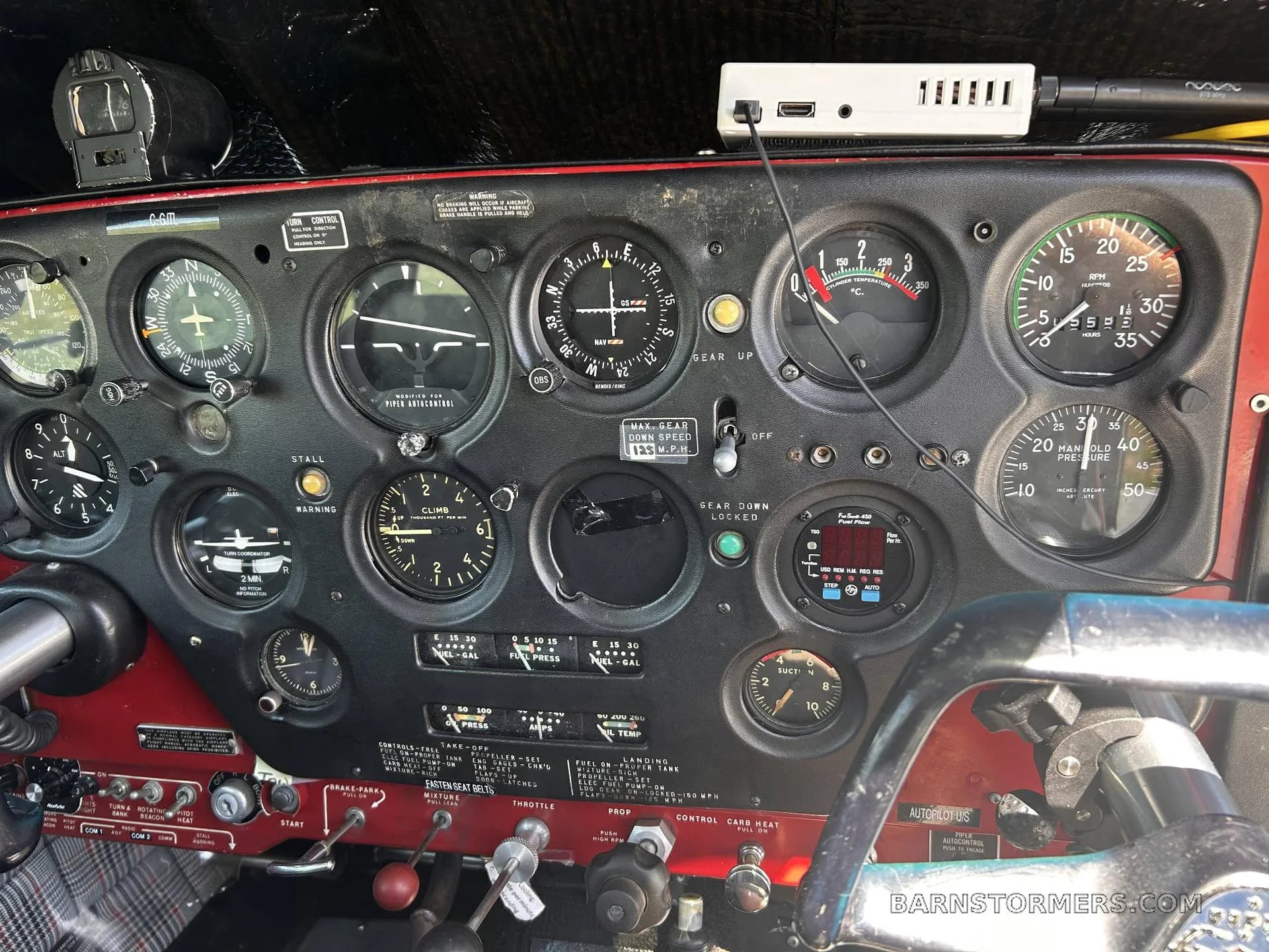 A close-up view of a vintage aircraft cockpit with numerous analog gauges and a modern USB hub.