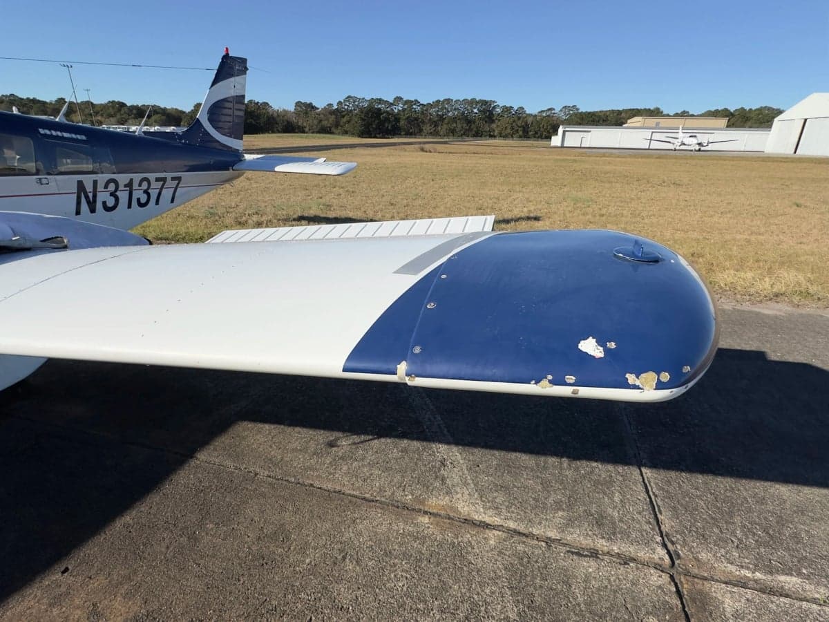 Close-up of the wingtip of a blue and white Piper Cherokee aircraft.