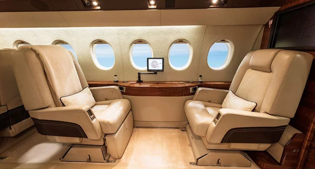 Two large, comfortable beige leather seats facing each other in the cabin of a business jet.