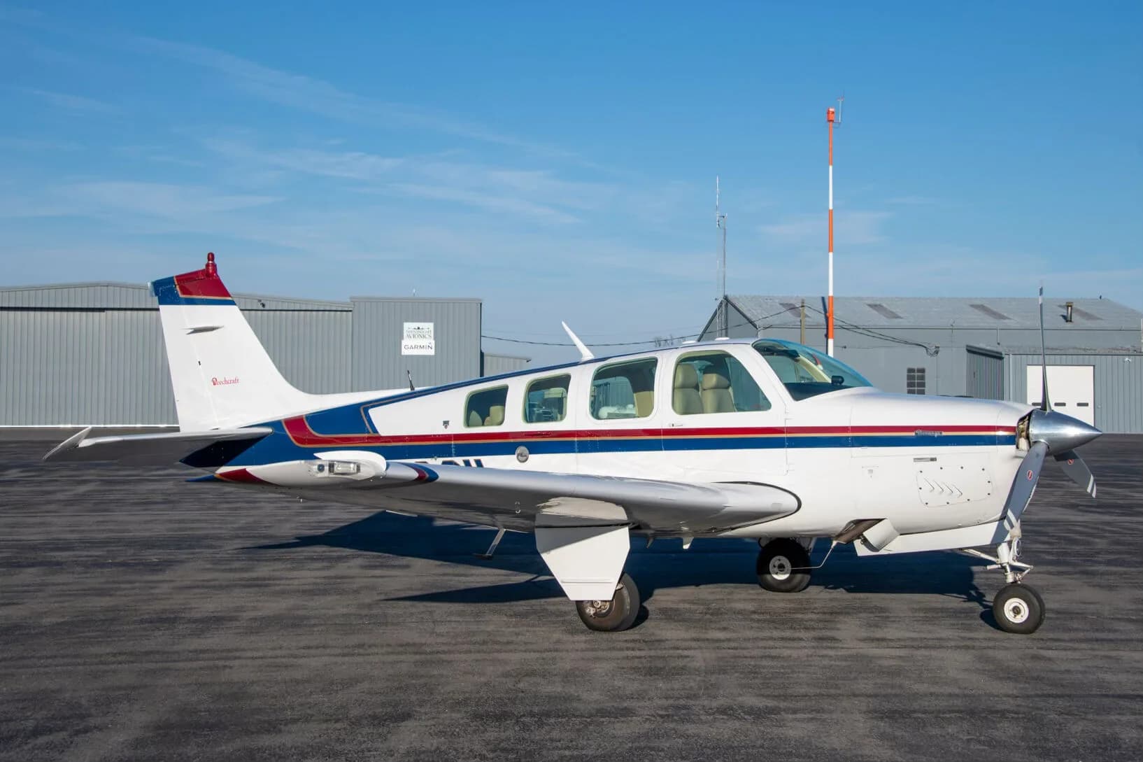 A white Beechcraft Bonanza N2261L with blue and red stripes parked on an airfield, viewed from the side.