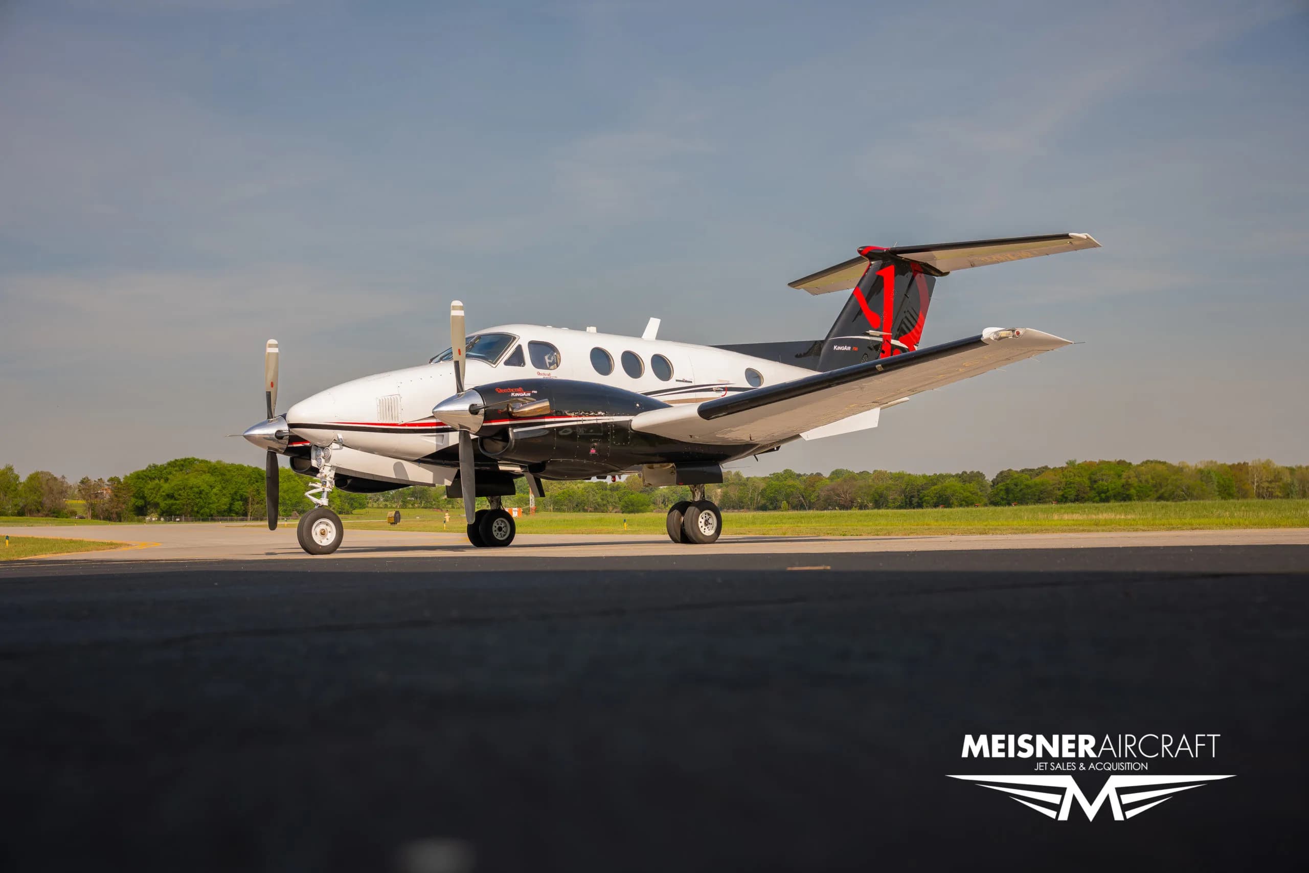 A white and black Beechcraft King Air with red tail accents parked on an airfield.