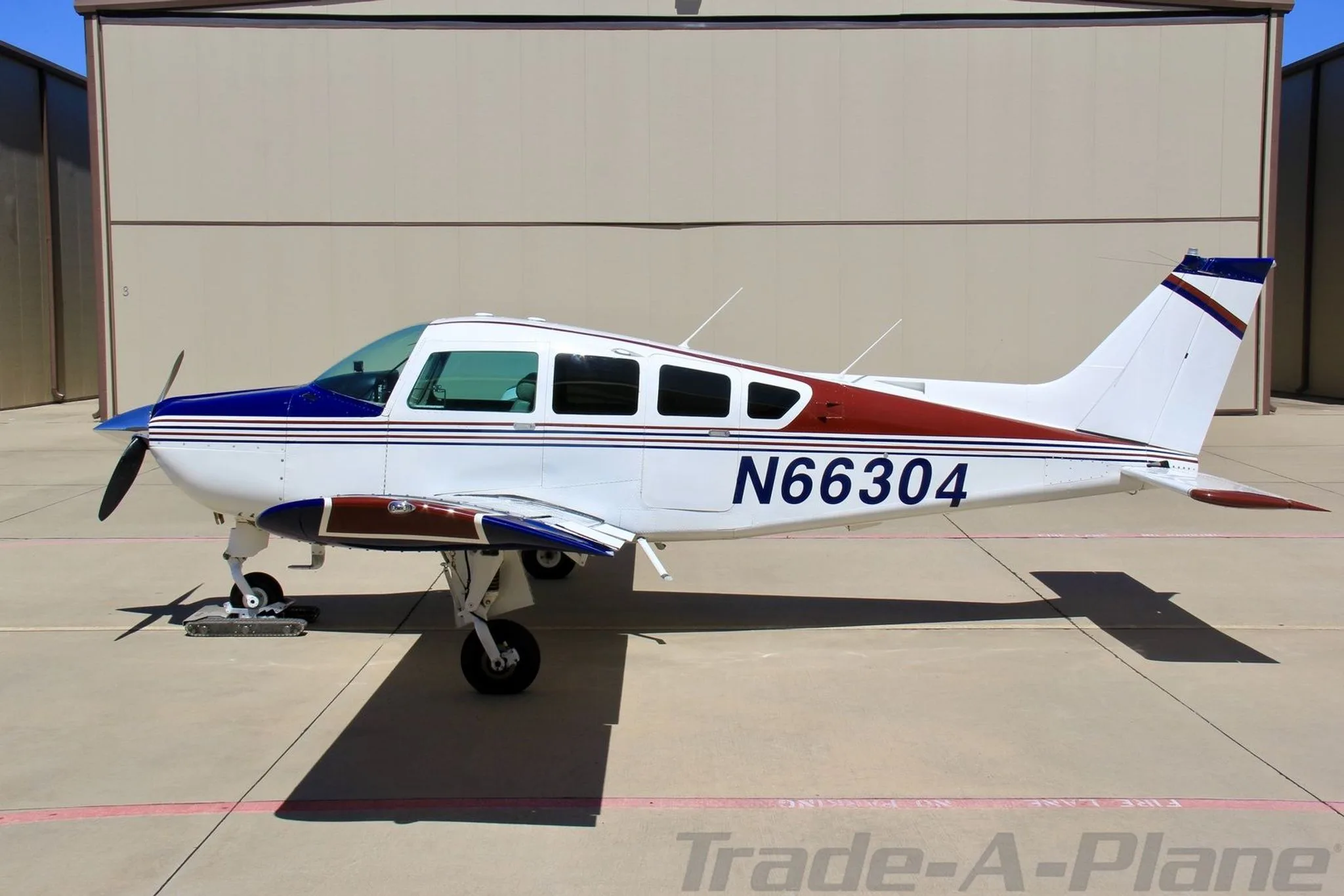 A full side view of the white, blue, and red single-engine aircraft N66304 parked on an apron.