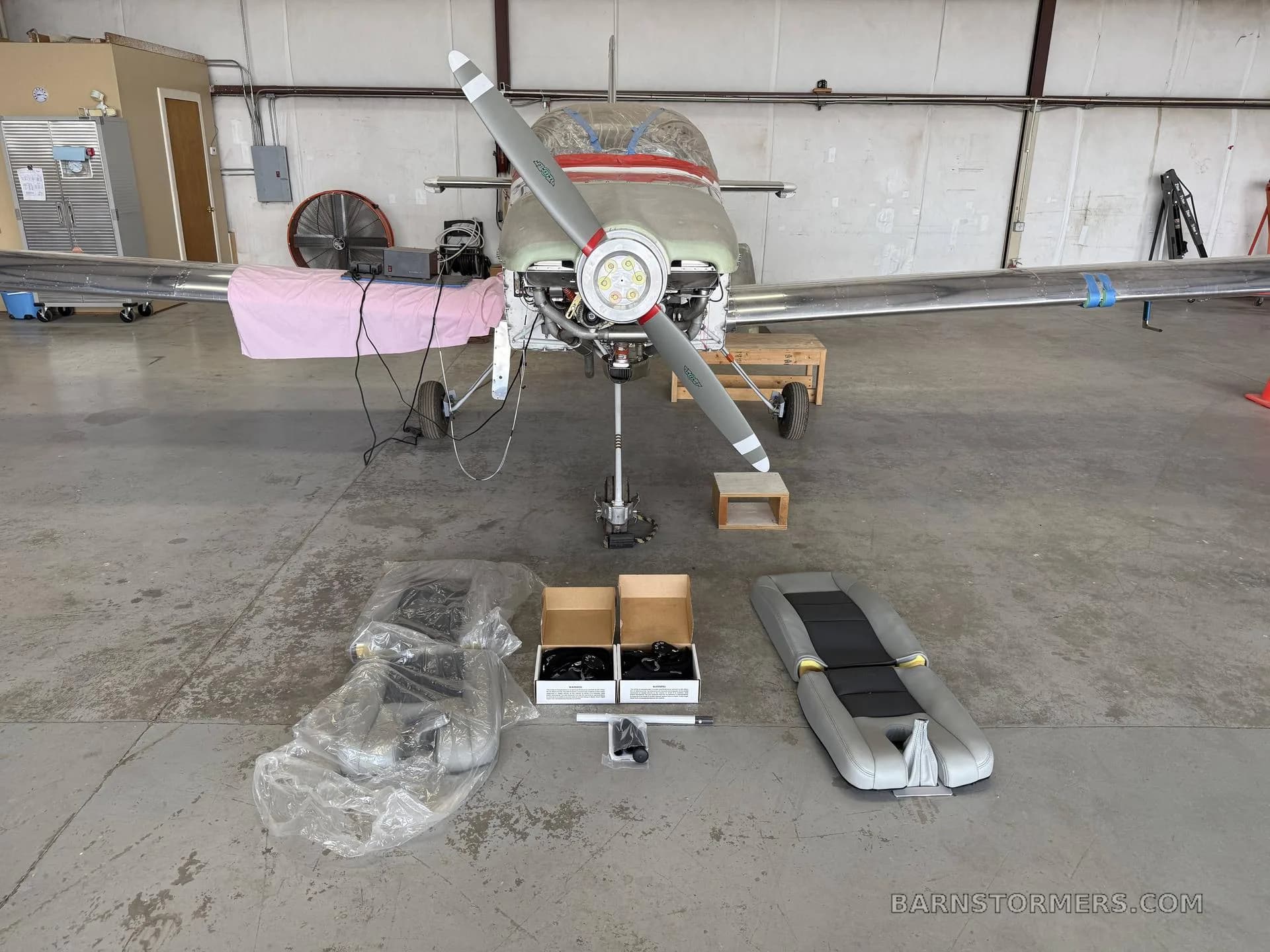 A front view of a partially assembled aircraft with new seat cushions and parts laid out on the hangar floor.
