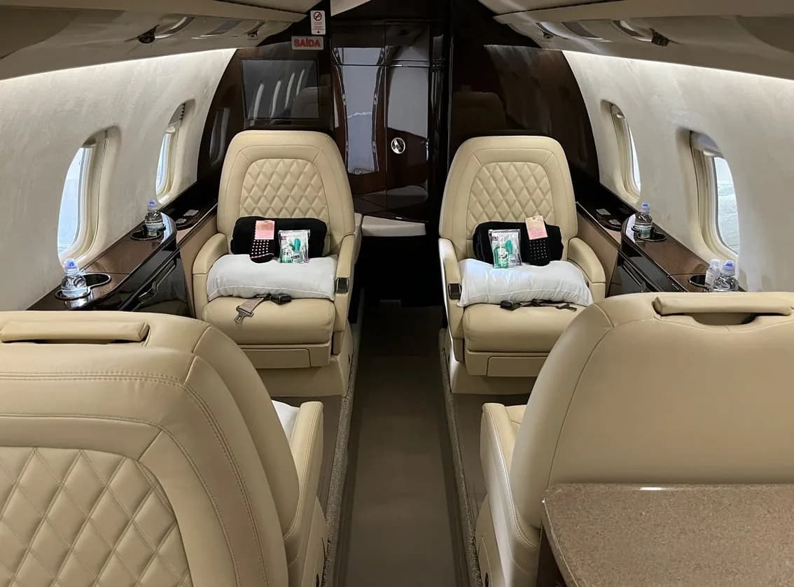 Two cream leather seats in the business jet cabin are adorned with pillows, blankets, and bottled water.