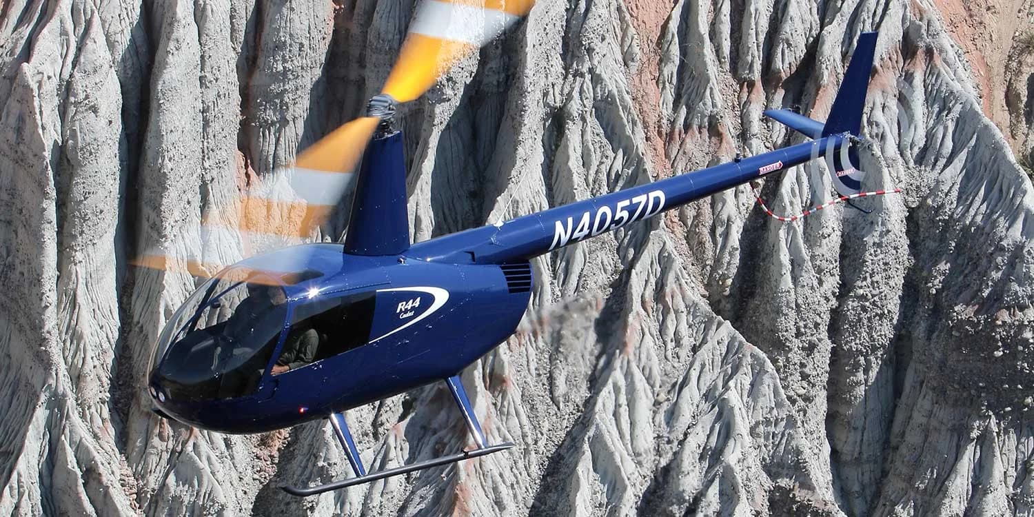 A blue Robinson R44 helicopter, registration N4057D, flies near a canyon wall.