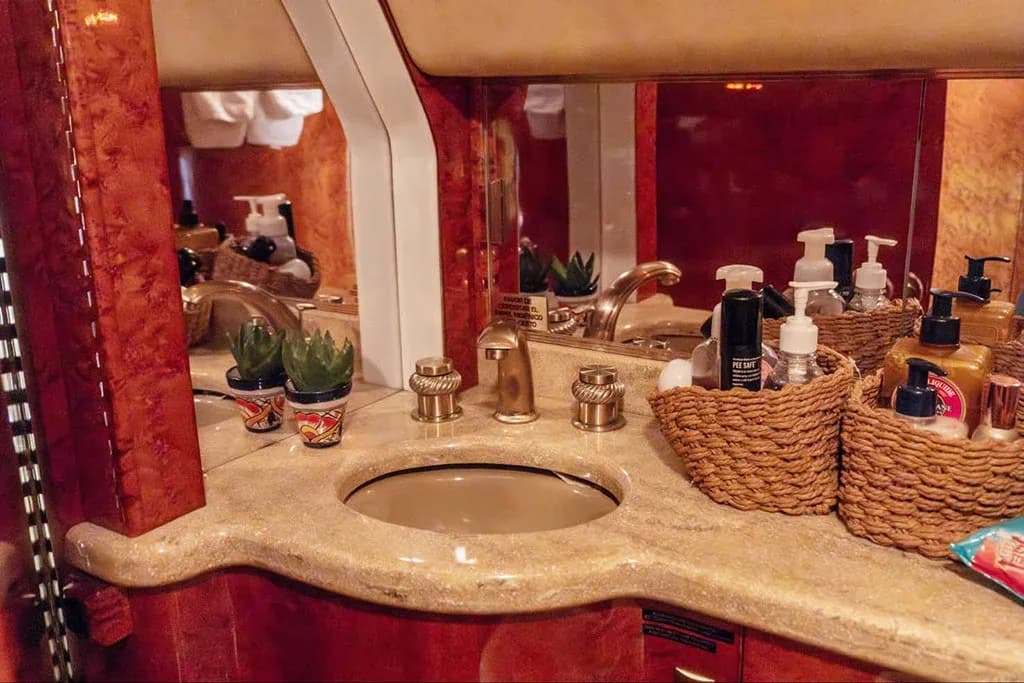 A private jet lavatory vanity with a sink, gold fixtures, and various toiletries.