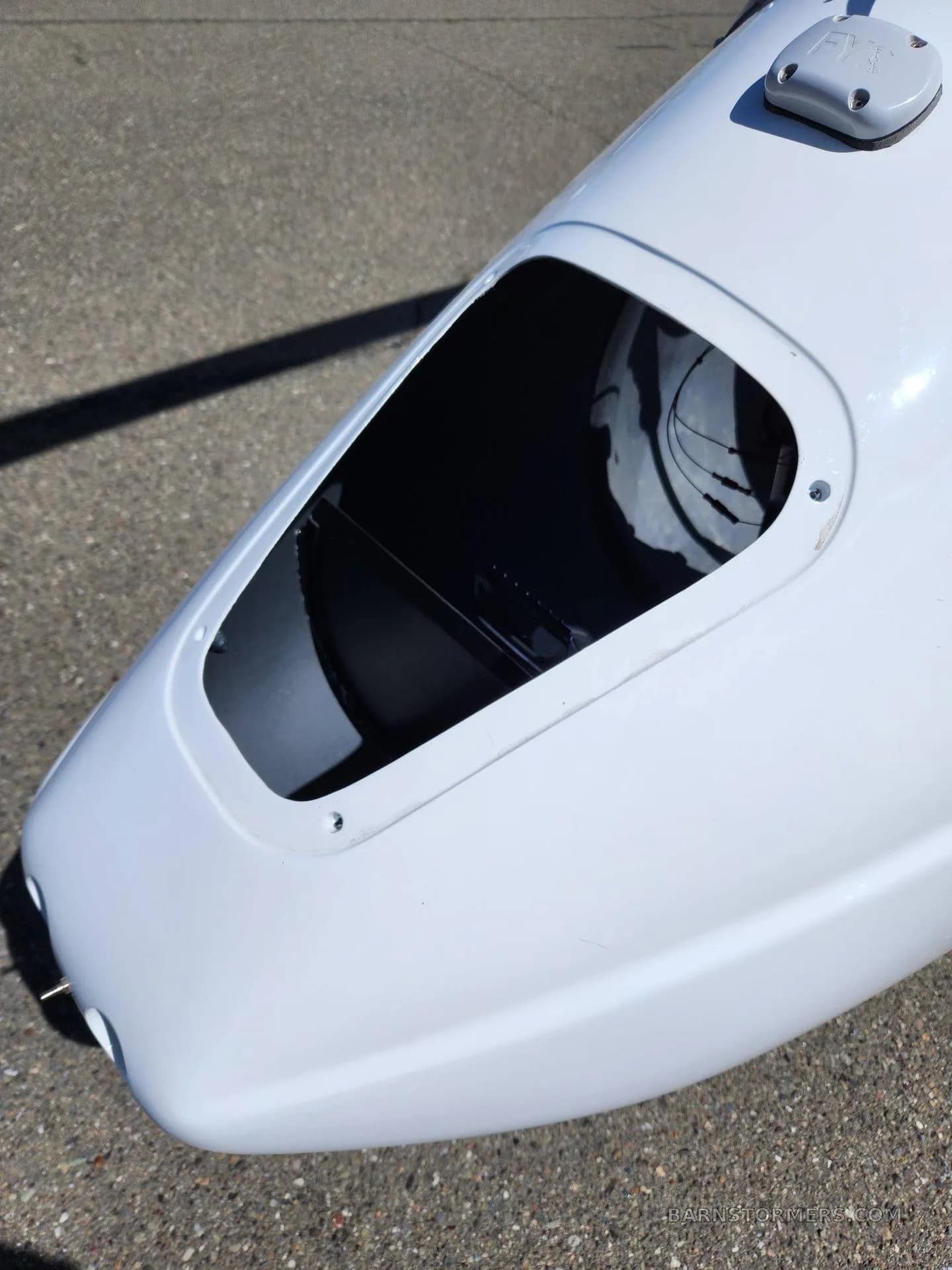 A close-up view of an open storage compartment or access panel on the white fuselage of a gyrocopter.