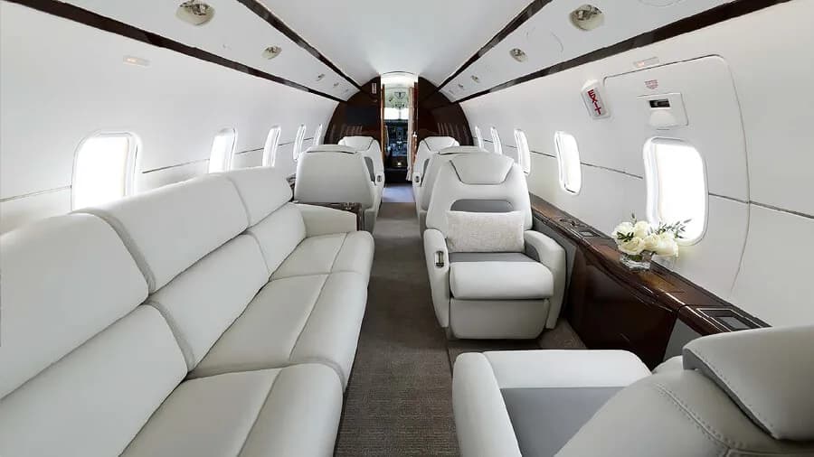 A wide view of the private jet cabin interior featuring a white leather sofa and individual seats.