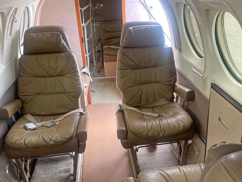 Two tan leather passenger seats in the aircraft cabin, with more seating visible further back.