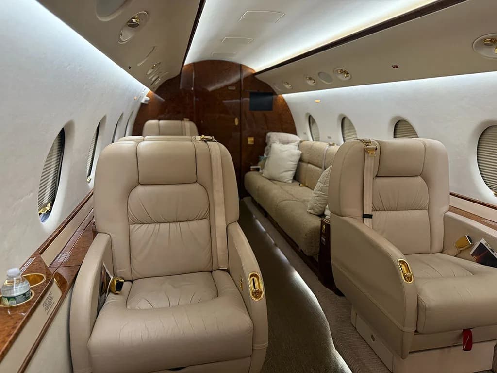 The elegant interior of a business jet cabin, featuring beige leather seats and a matching sofa.