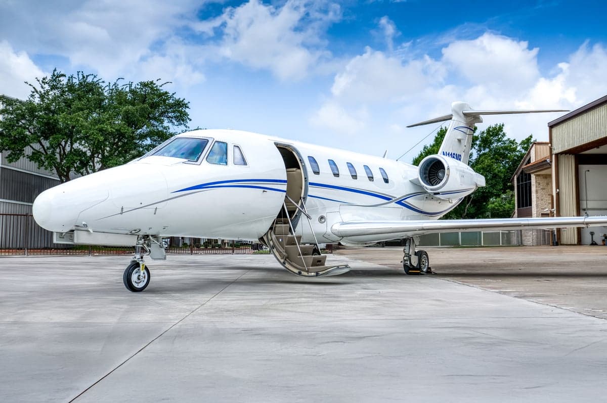 A white jet with blue accents is parked on the tarmac with the door open.