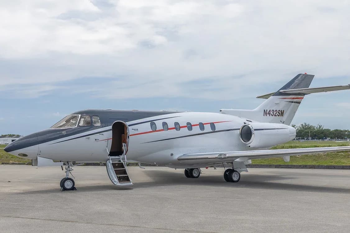 A white and black business jet, registration N432SM, with its passenger door open and stairs extended, parked on an airfield.