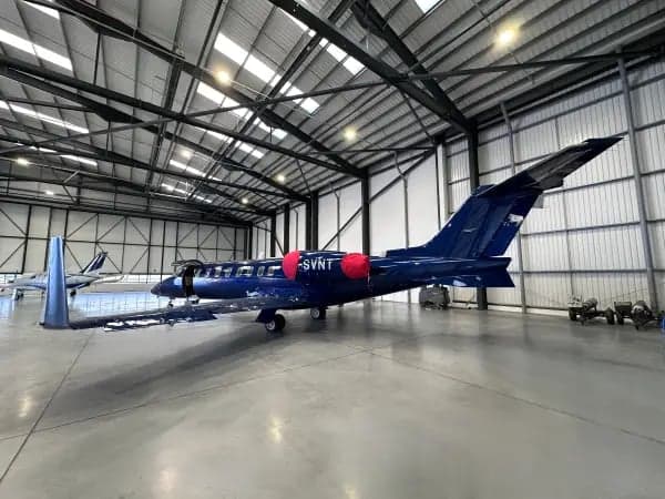 A dark blue Learjet is parked inside a hangar, with red engine covers.