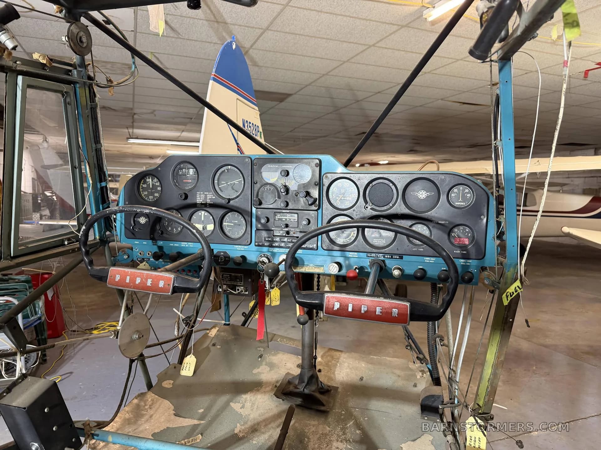 A close-up view of a Piper aircraft's dual control yokes and instrument panel in a hangar.