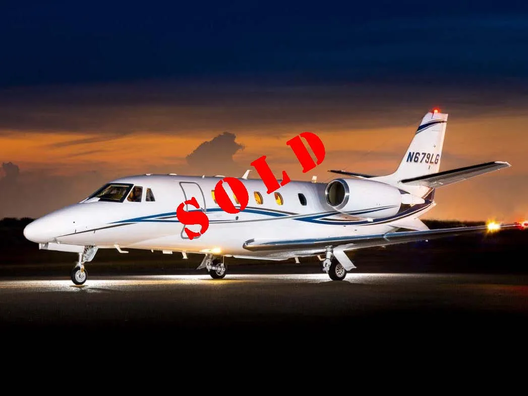 A white business jet with blue and gold stripes, registration N679LG, parked on an airfield at dusk.
