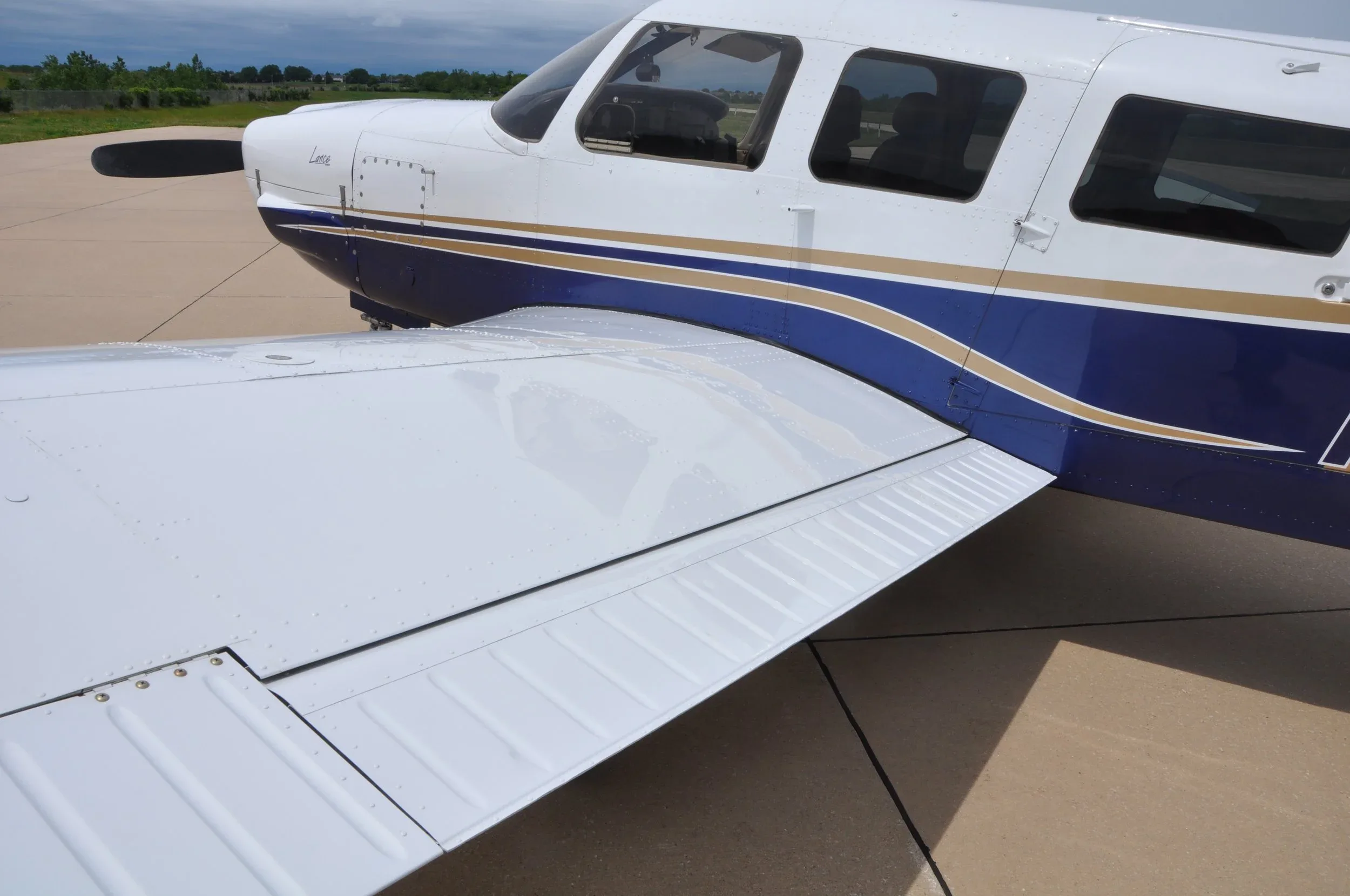 A close-up view of the white wing and blue fuselage of the Piper Lance aircraft.