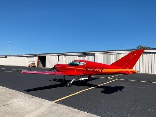 A red aircraft with registration N54JX parked in front of a hangar.