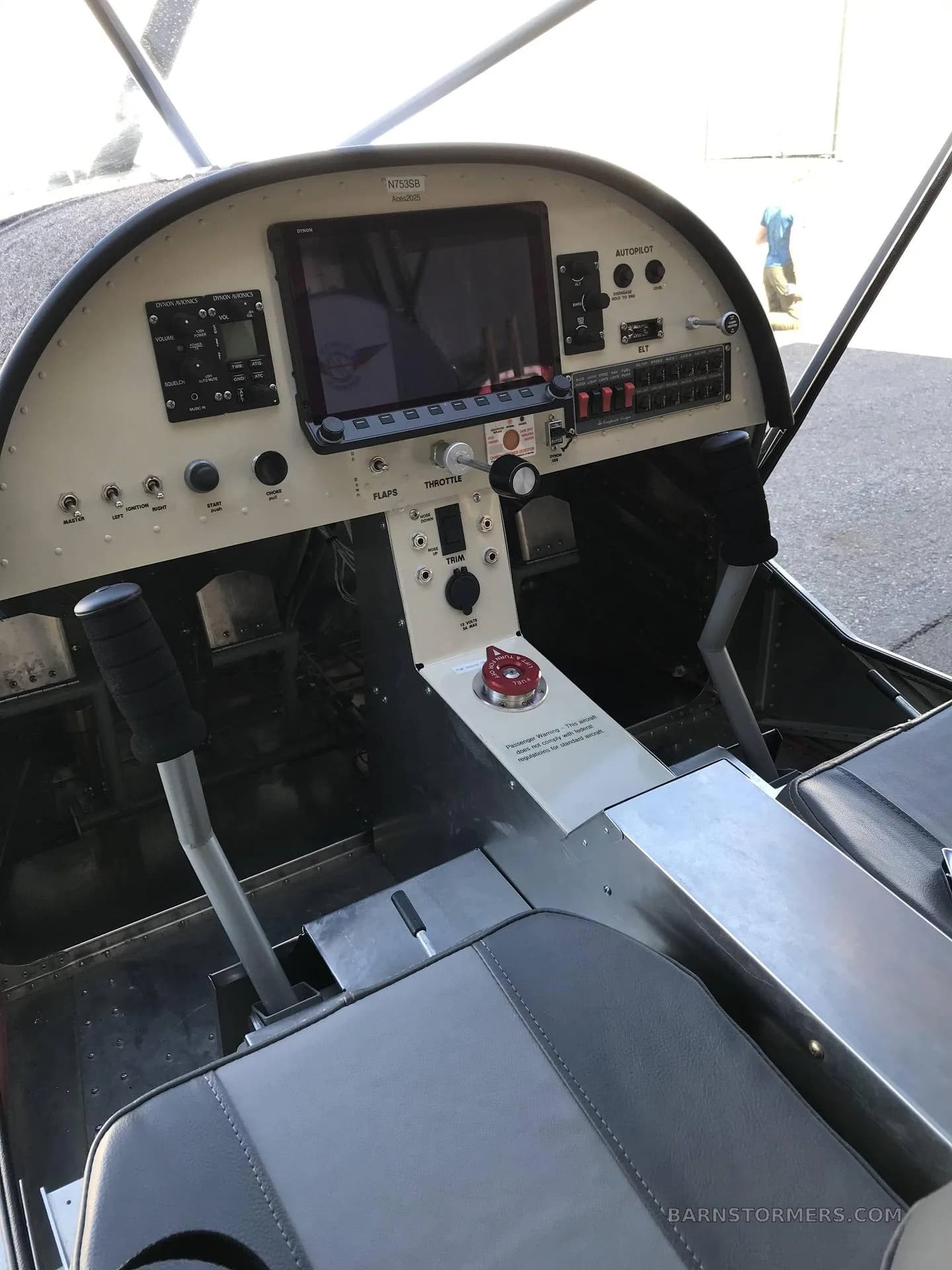 A view of the cockpit interior of a light aircraft, showing the instrument panel, control sticks, and two grey seats.