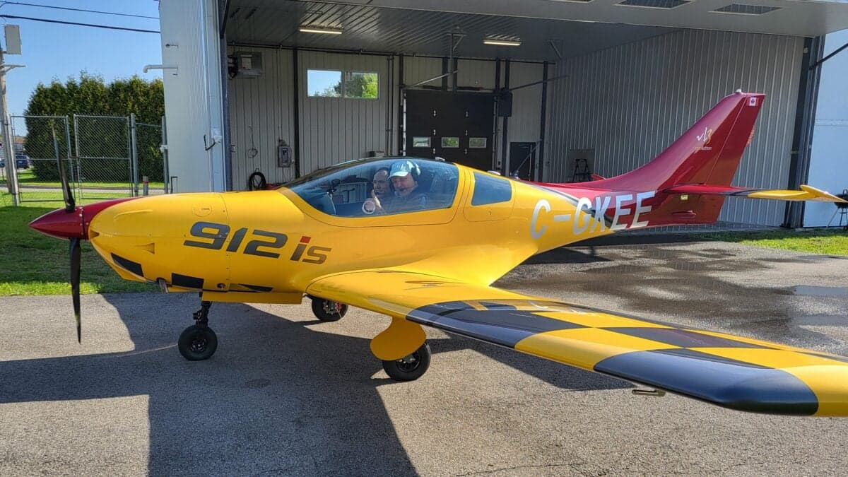Side view of a yellow and red VL3 Evolution aircraft parked outside a hangar.
