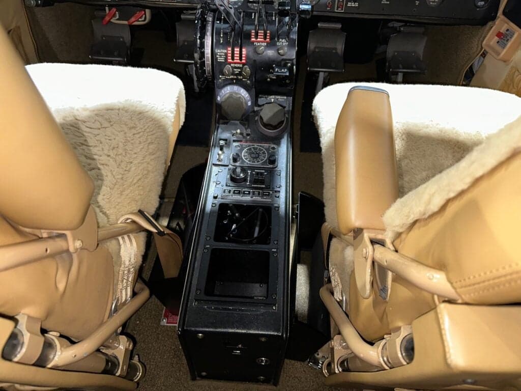 A close-up view of the center console and tan sheepskin-covered pilot seats in the aircraft cockpit.