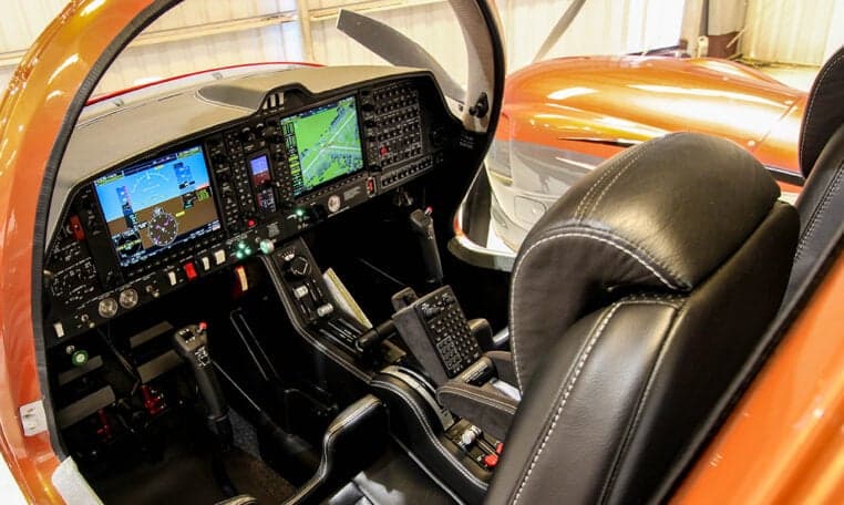 The cockpit of a Diamond DA62 aircraft features a modern glass panel display and black leather seats.
