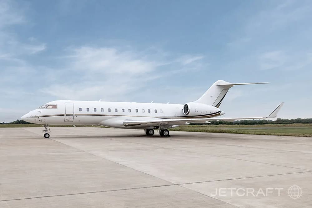A white Bombardier Global business jet with gold and black stripes seen from the side on an airfield.