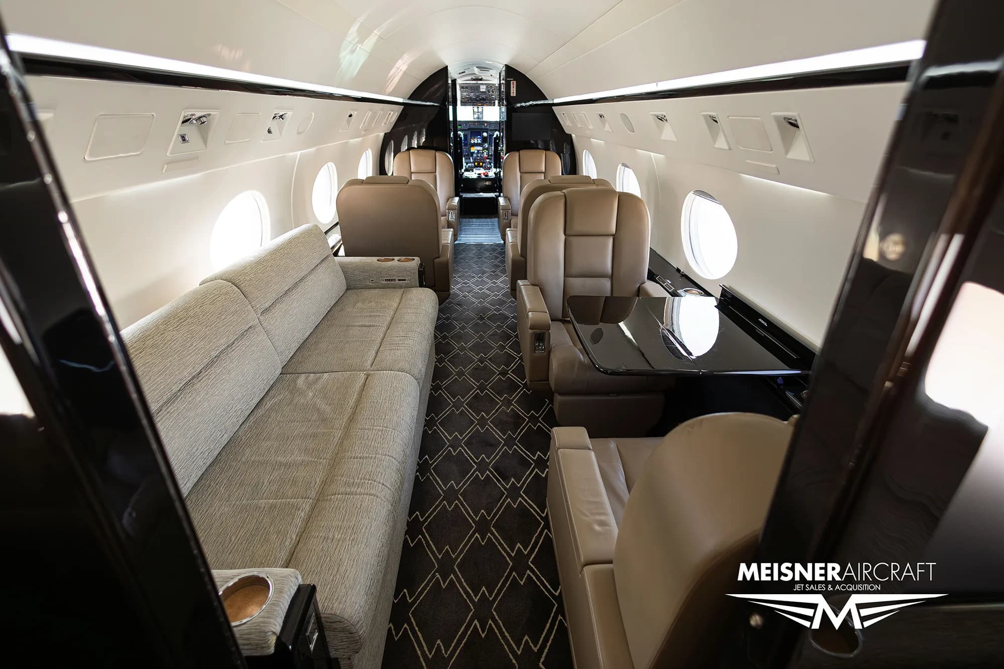 Spacious aircraft cabin interior with a sofa and leather seats.