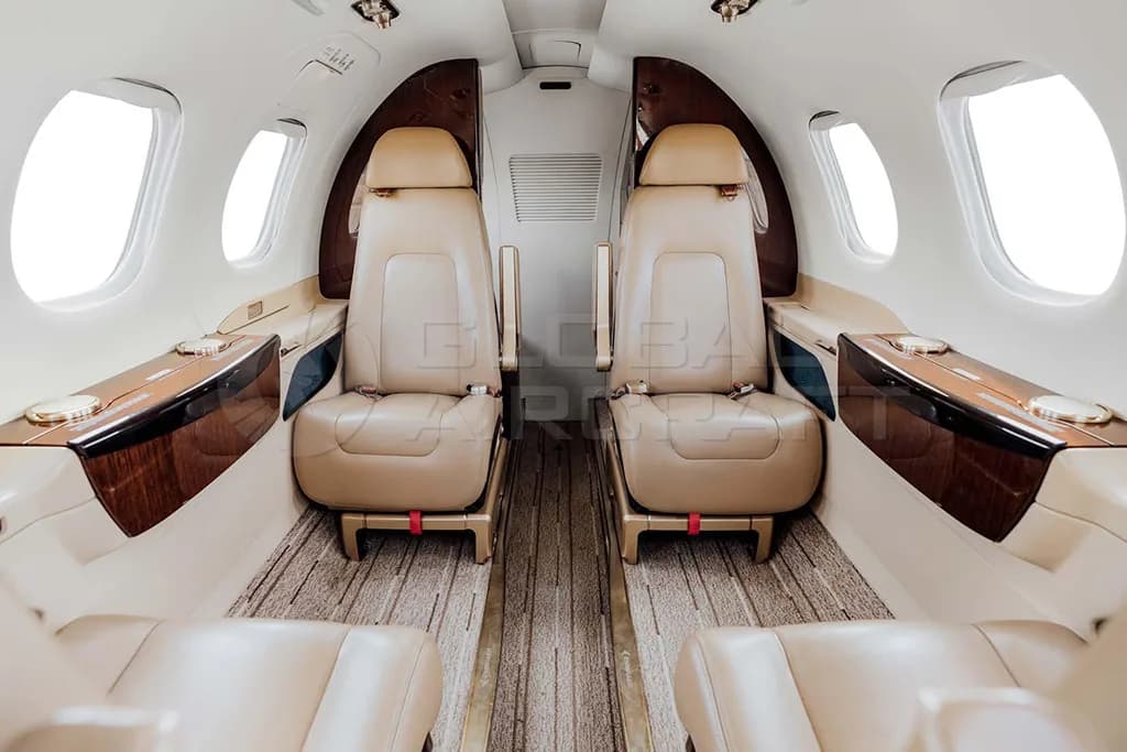 The interior cabin of an Embraer Phenom 300, featuring two rows of beige leather seats and wood trim.