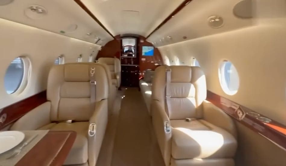 The luxurious interior cabin of a business jet, featuring tan leather seats and polished wood accents.