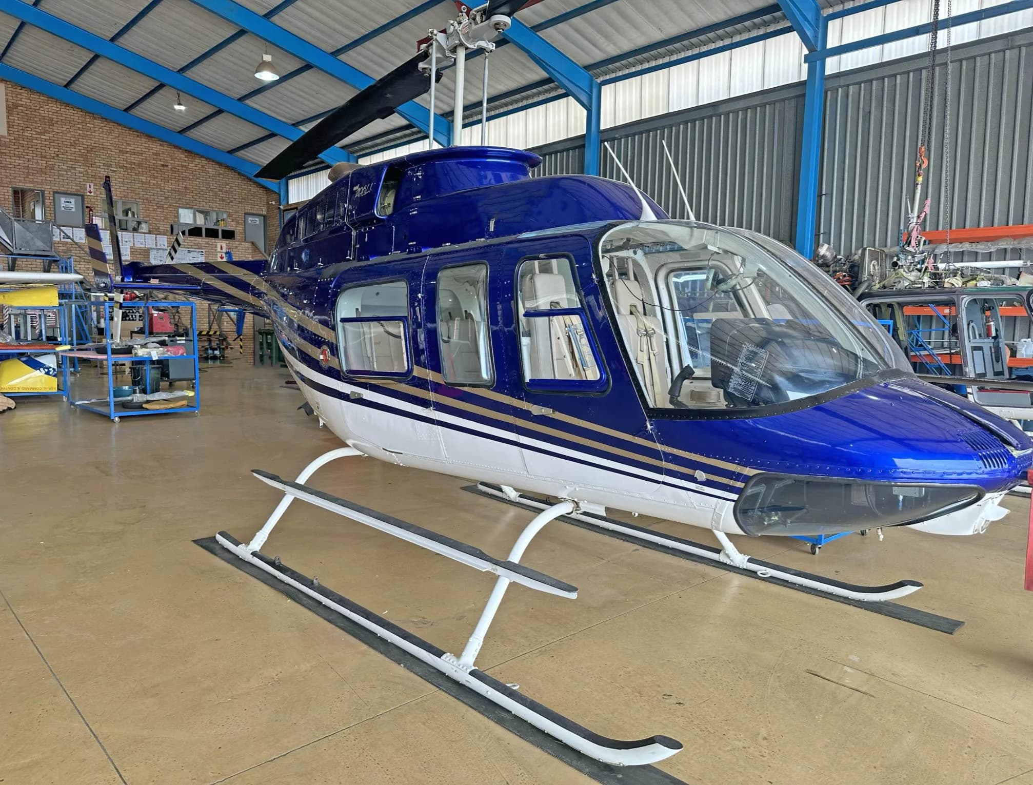 A blue and white Bell 206L-4 LongRanger helicopter with gold stripes parked inside a hangar.