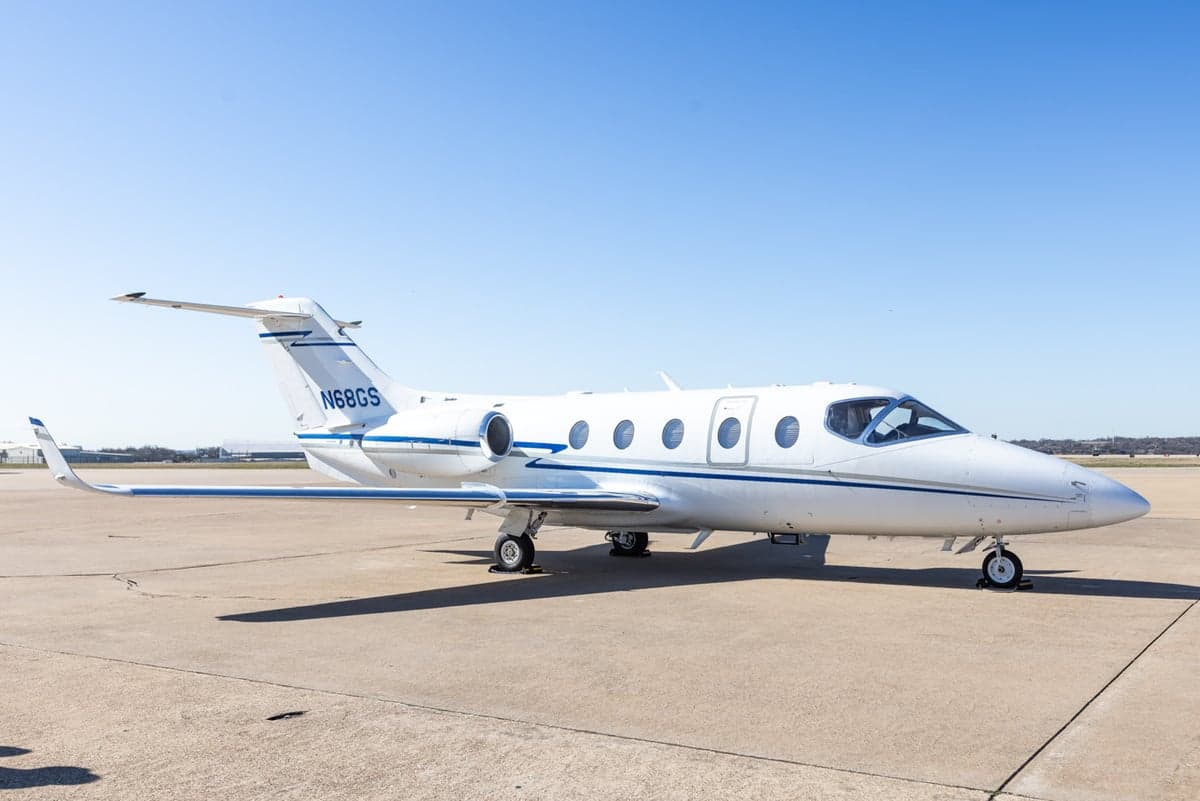A white Learjet 45XR with blue stripes is parked on the tarmac.