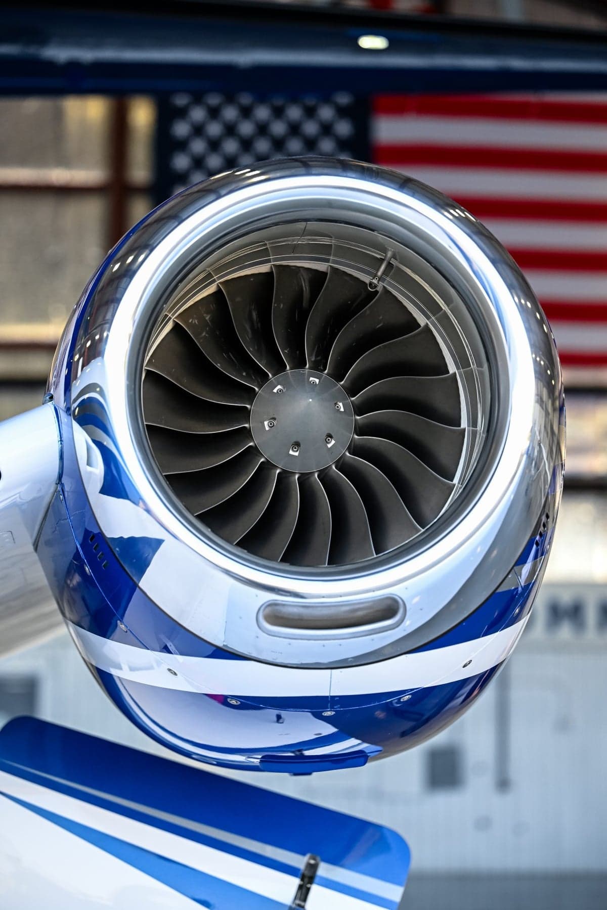 Close-up view of the polished jet engine intake with blue and white paint scheme, inside a hangar.