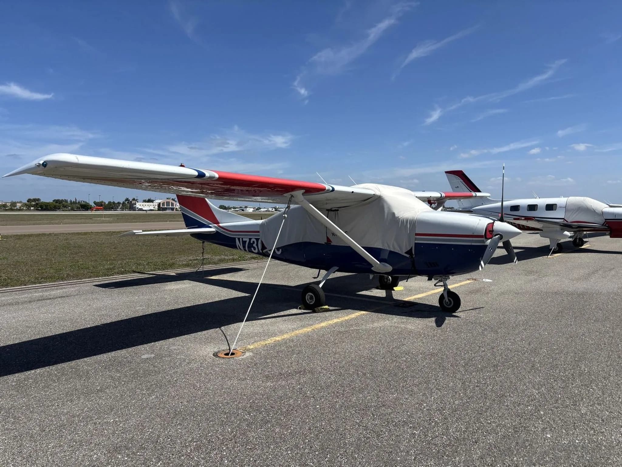 A white, blue, and red Cessna N7360C parked on an airfield with engine and cockpit covers.