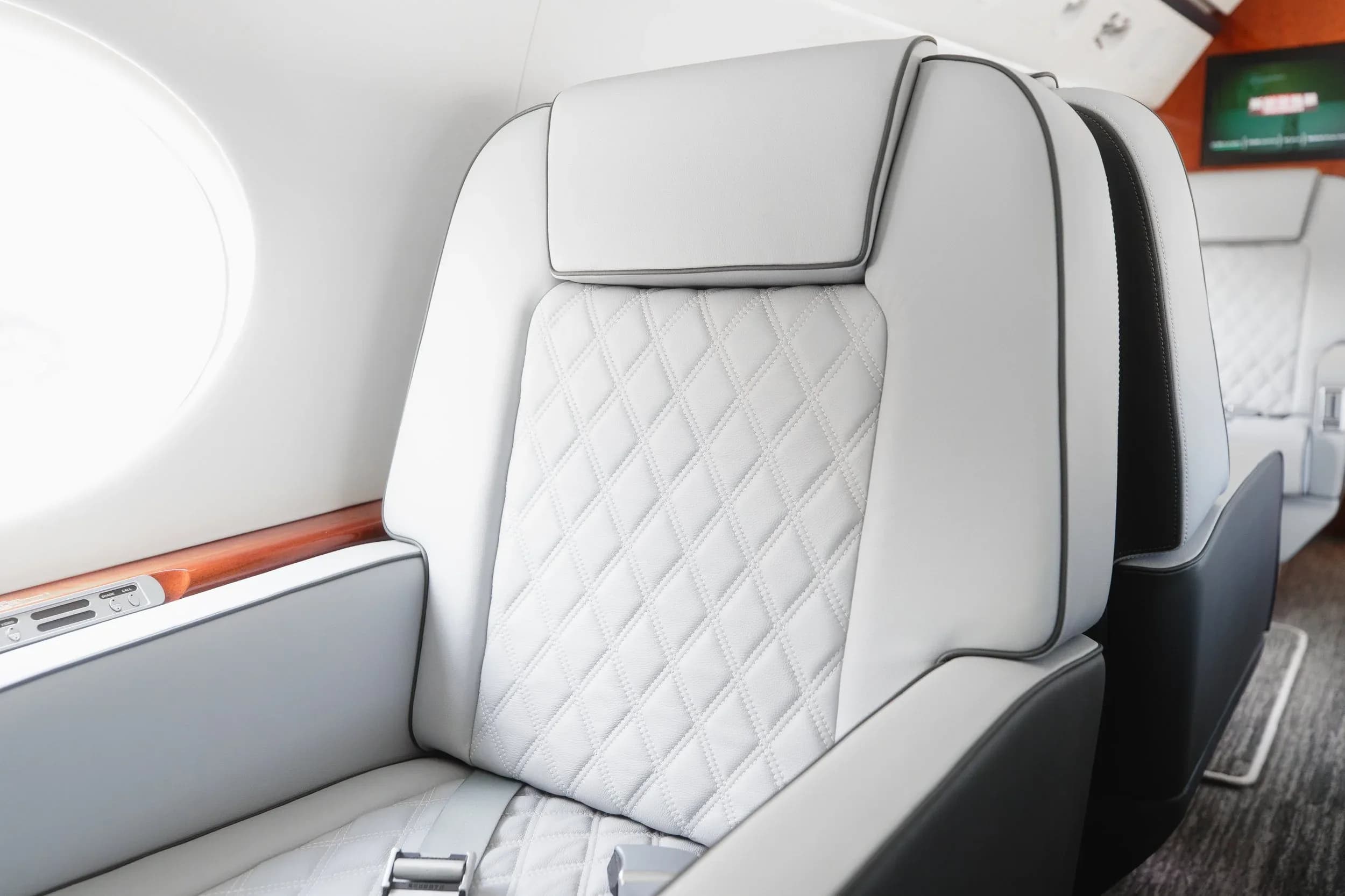A detailed close-up of a light gray quilted leather seat with dark gray piping in the private jet's cabin.