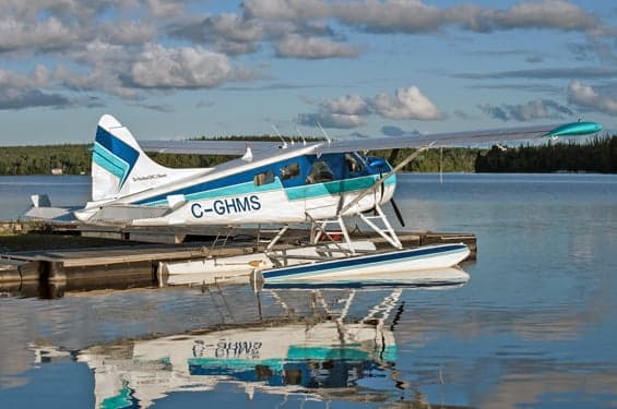 De Havilland DHC-2 Beaver floatplane in white and blue livery, docked on a lake.