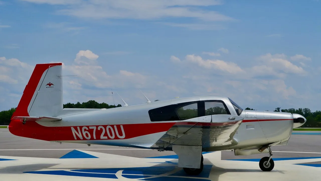 Left side view of a silver and red Mooney aircraft with registration N6720U on an airfield.