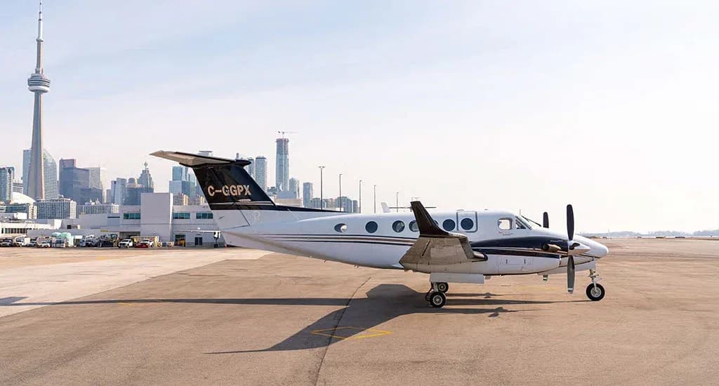 A white and black twin-engine turboprop aircraft (King Air) with tail number C-GGPX parked on an airfield with the Toronto skyline in the background.