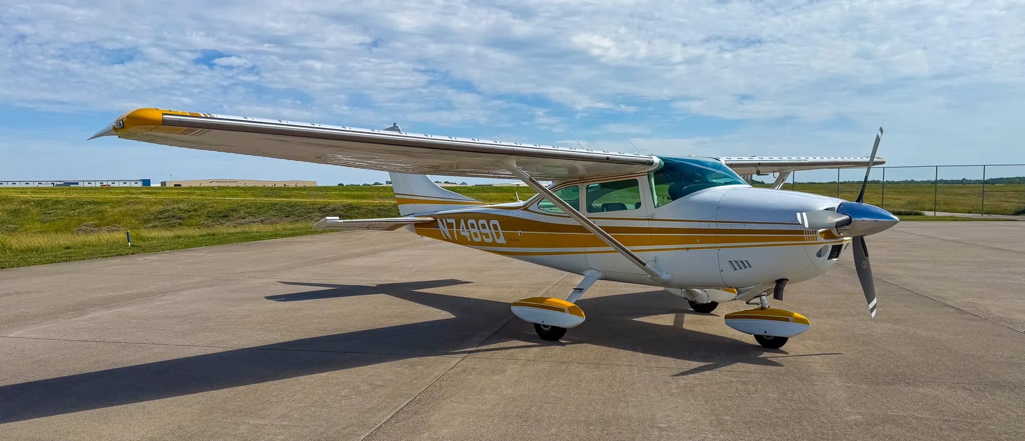 A white and gold Cessna Skylane N7489Q is parked on an airfield tarmac, viewed from the front-left side.