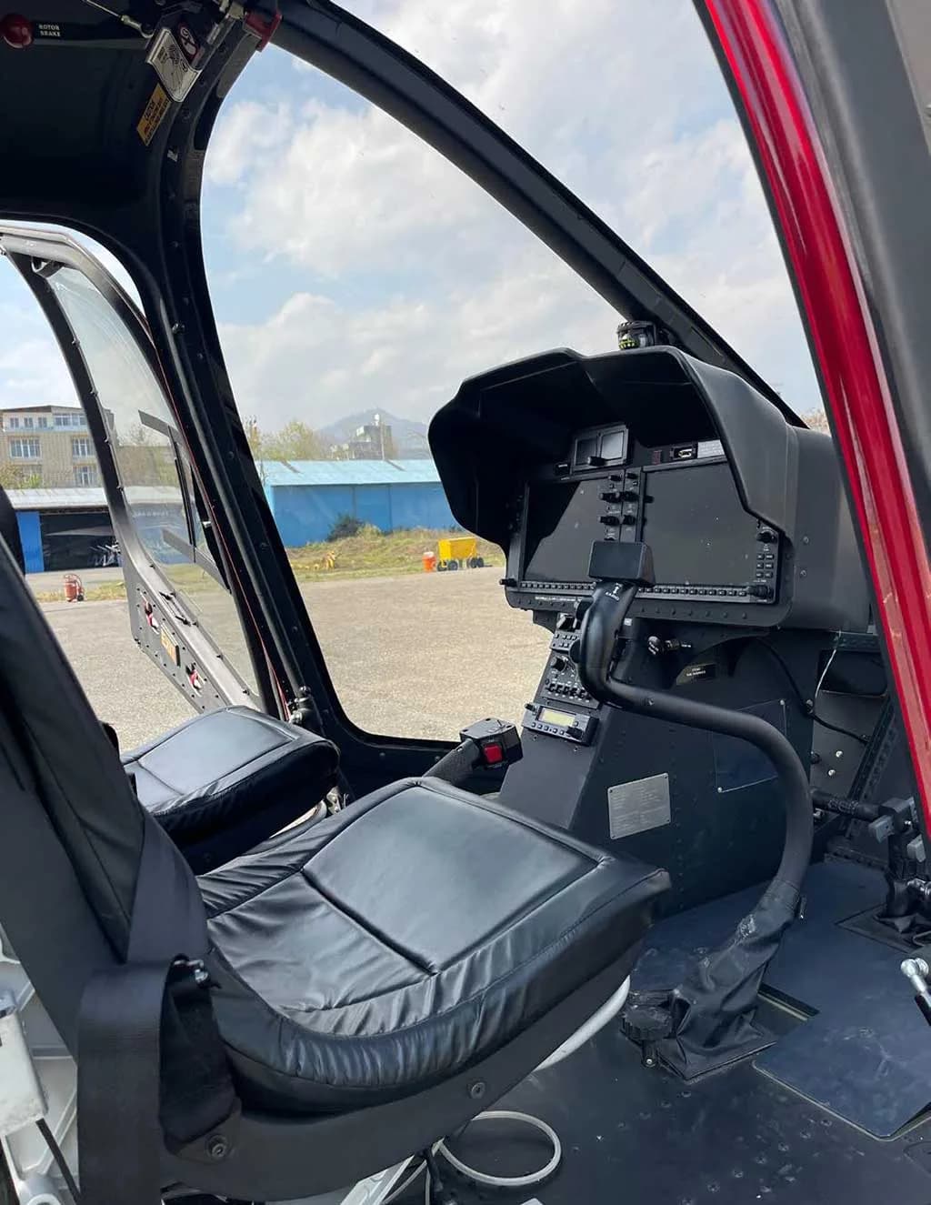 The helicopter cockpit features a black pilot's seat and a modern instrument panel with screens.