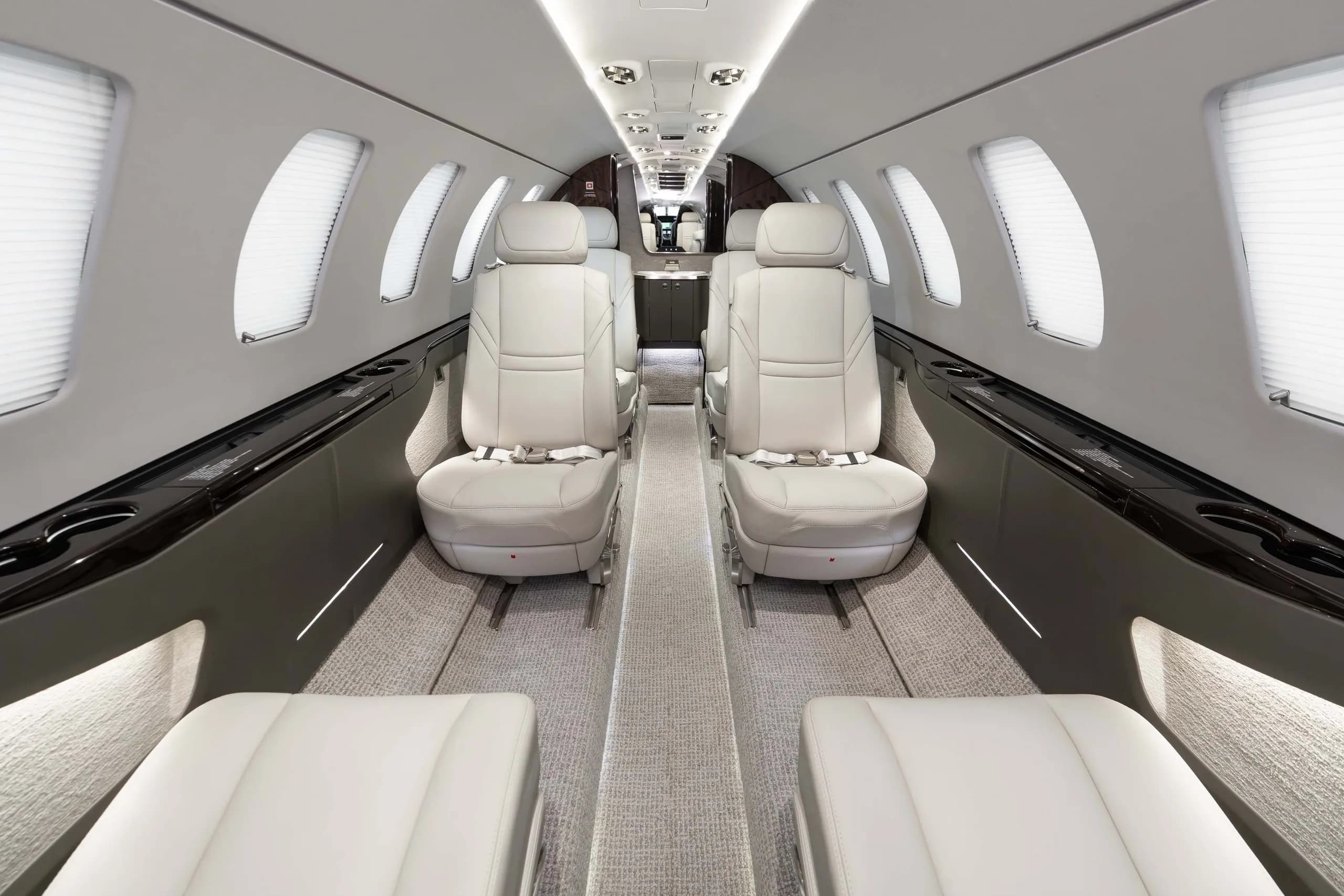 The luxurious interior cabin of a business jet with light grey leather seats and carpet, looking towards the rear.