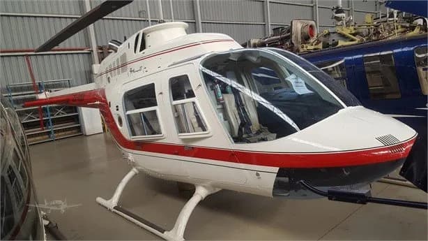 Side view of a Bell Jet Ranger helicopter with red and white paint scheme inside a hangar.