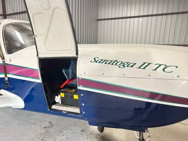 Close-up of the Piper Saratoga II TC fuselage with the cargo door open, revealing a storage compartment.