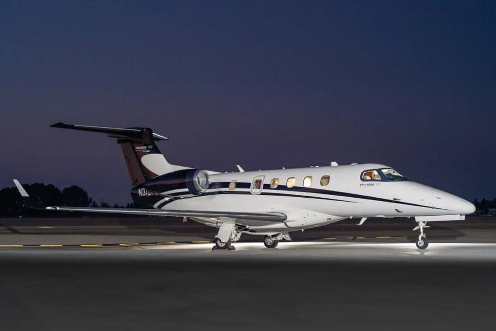 A Phenom 300 aircraft with a white and black paint scheme is parked on the tarmac at night.