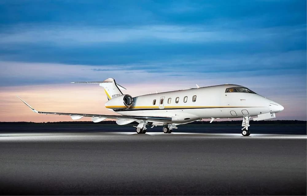A white N157PH business jet with yellow and grey stripes is parked on an airfield at dusk.