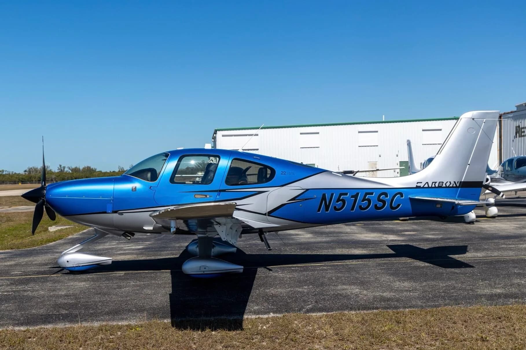 A side view of a blue and silver Cirrus SR22 aircraft (N515SC) parked on an airfield with a building in the background.