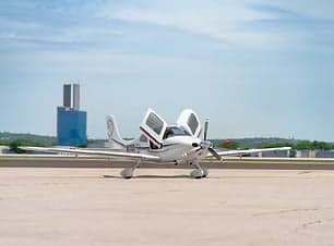 A Cirrus SR22 aircraft is parked on the tarmac with its doors open.