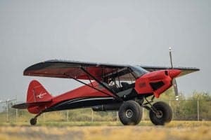 Side view of a red and black Carbon Cub aircraft on the ground.
