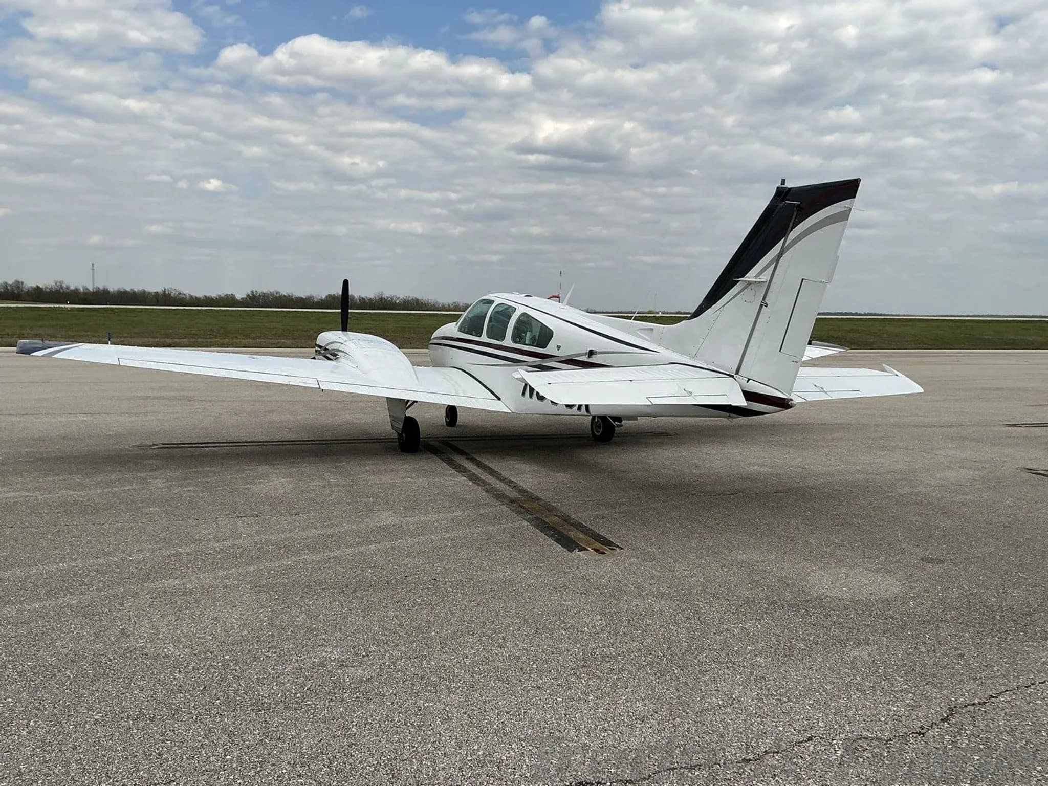 A rear-side view of a white twin-engine propeller aircraft with black and maroon stripes parked on an asphalt tarmac.