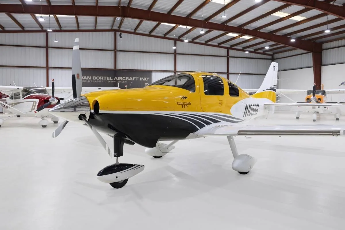 A yellow and white Cessna TTx (N105RG) with black accents, parked in a hangar, viewed from the front-left side.